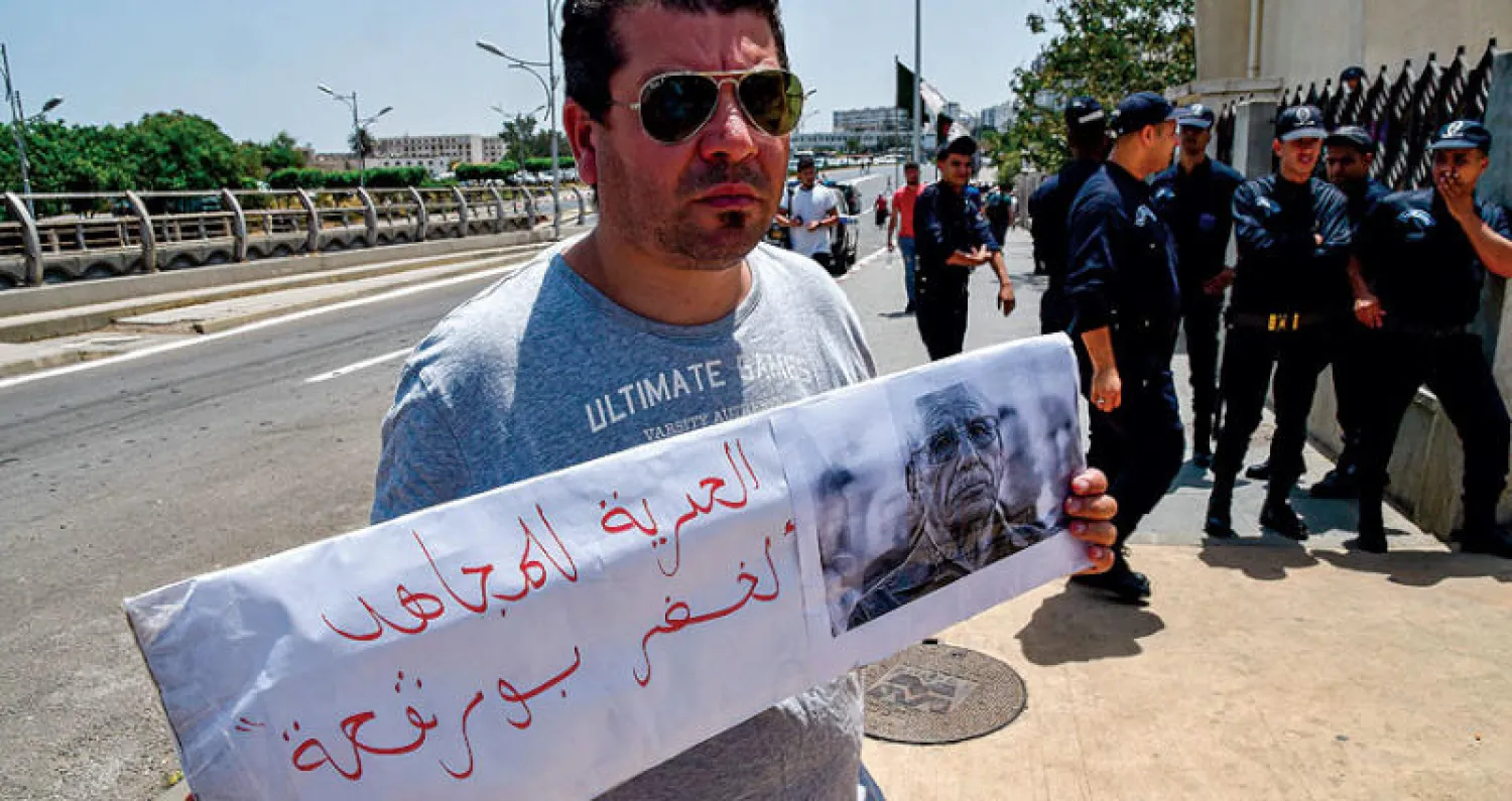 جزائري يرفع لافتة أمام محكمة في العاصمة الأسبوع الماضي  تضامناً مع الرائد لخضر بورقعة المتهم بـ«محاولة إضعاف معنويات الجيش» (أ.ف.ب)