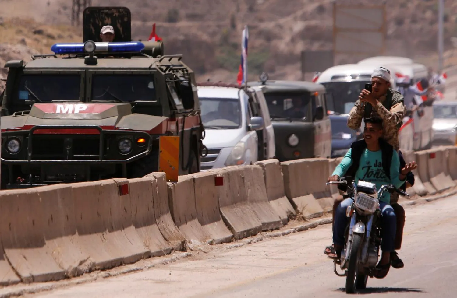 A Syrian soldier takes selfies pictures as Russian military vehicle is seen in convoy during re-opening the road between Homs and Hama in Rastan, Syria June 6, 2018. REUTERS/ Omar Sanadiki

