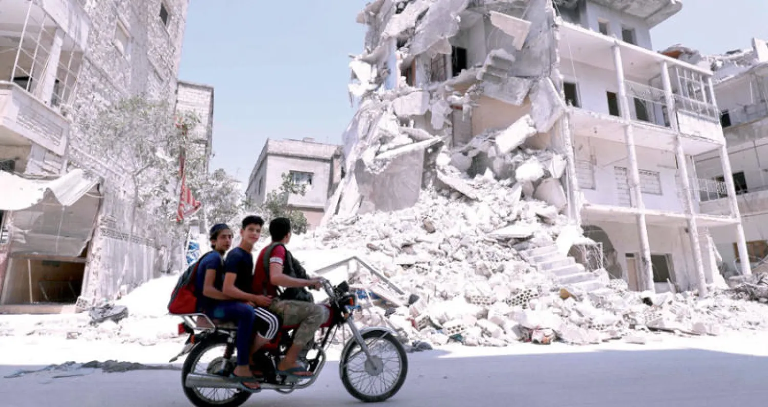 شبان على دراجة يمرون امام أبنية طالها الدمار في أريحا بإدلب أمس (أ.ف.ب)