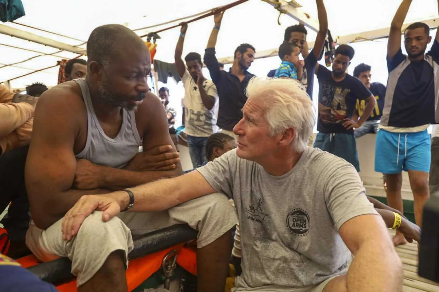 Actor Richard Gere, right, talks with migrants aboard the Open Arms Spanish humanitarian boat as it cruises in the Mediterranean Sea, Friday, Aug. 9, 2019. (AP Photo/Valerio Nicolosi)