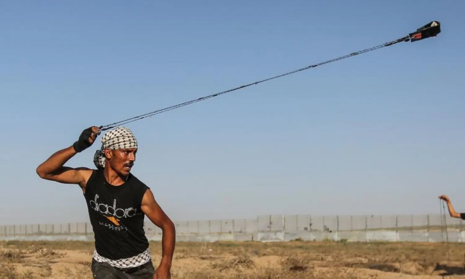 فلسطيني يلقي حجراً نحو الجانب الإسرائيلي من السياج الفاصل في قطاع غزة (أ.ف.ب)