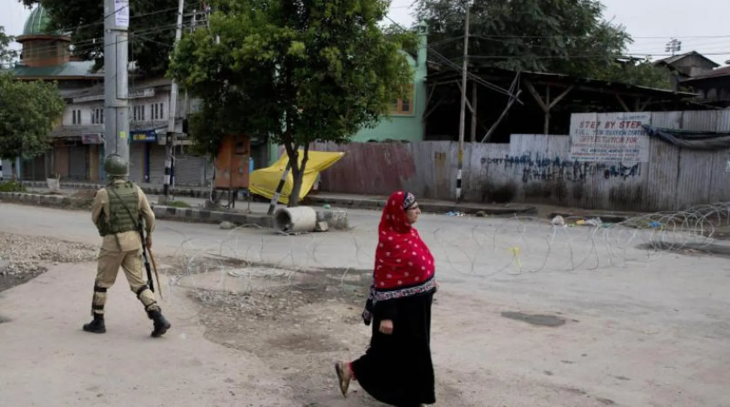 Keşmir'de bir kadın dikenli tellerle engellenmiş yolda Hindistan askerinin yanında yürüyor (AP)