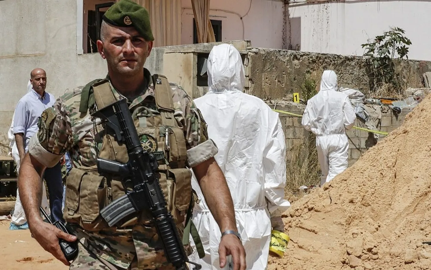 A Lebanese army soldier walks past military intelligence forensic investigators ar the scene where two drones came down in the vicinity of a media center of Hezbollah | AFP