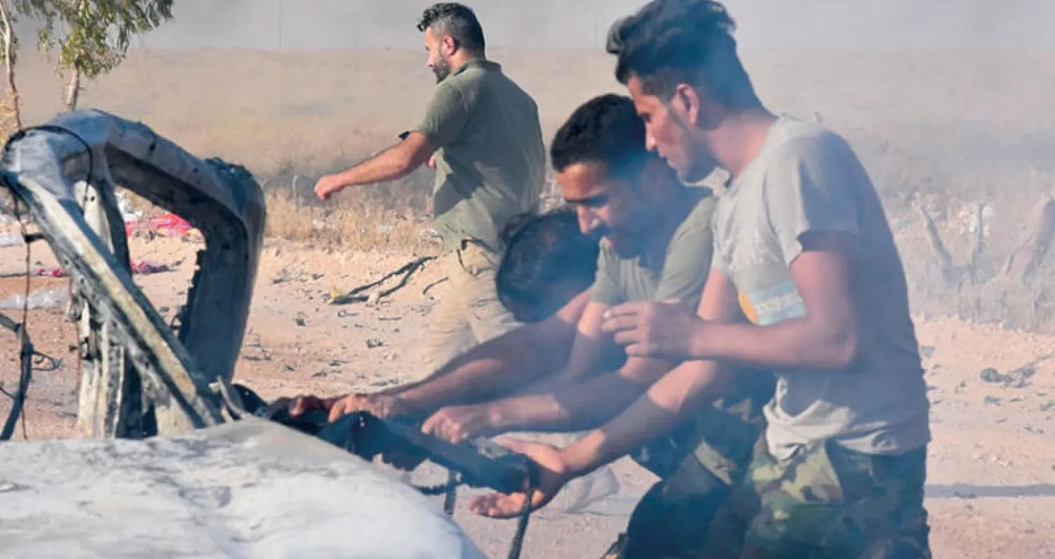 عناصر في «الحشد الشعبي» يحاولون إخراج جثة من مركبة  استهدفها قصف بطائرة «درون» في القائم على الحدود مع سوريا أمس (أ.ب)