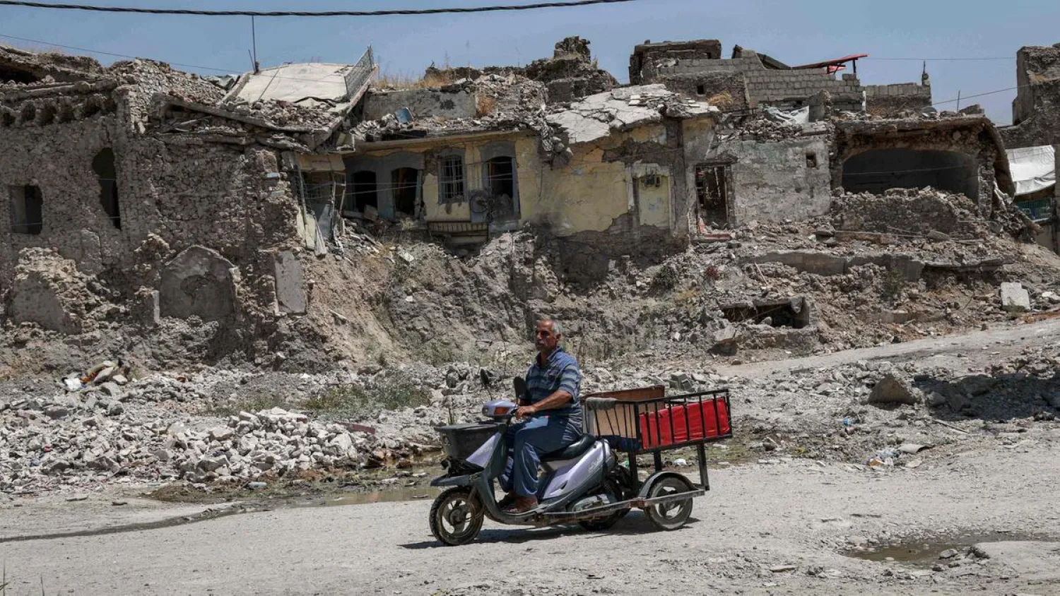 A man rides a scooter cart along a damaged street in the western part of Iraq's northern city of Mosul on August 10, 2019 | AFP