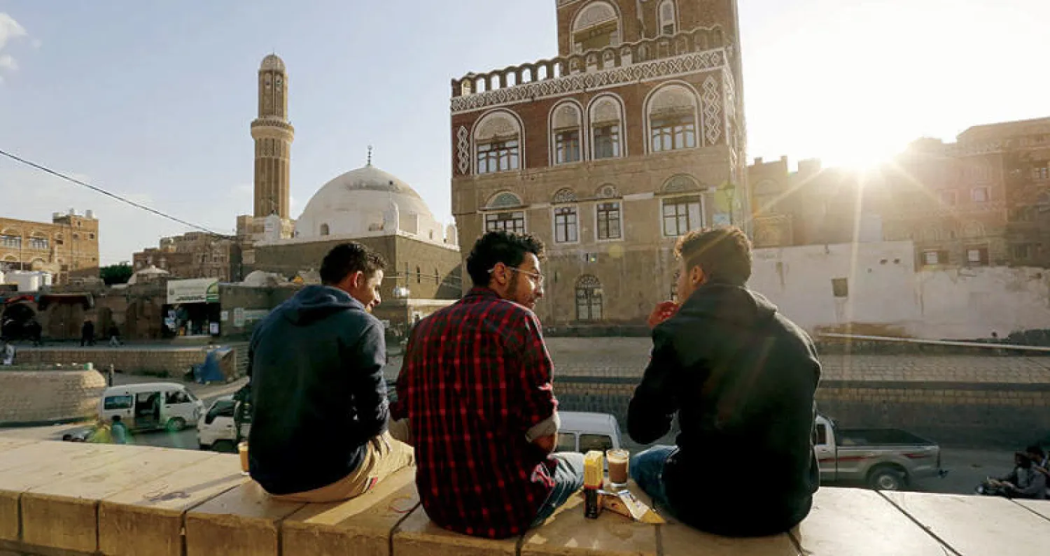 شبان يتحدثون ويظهر من أمامهم أحد مباني المدينة القديمة في صنعاء (إ.ب.أ)