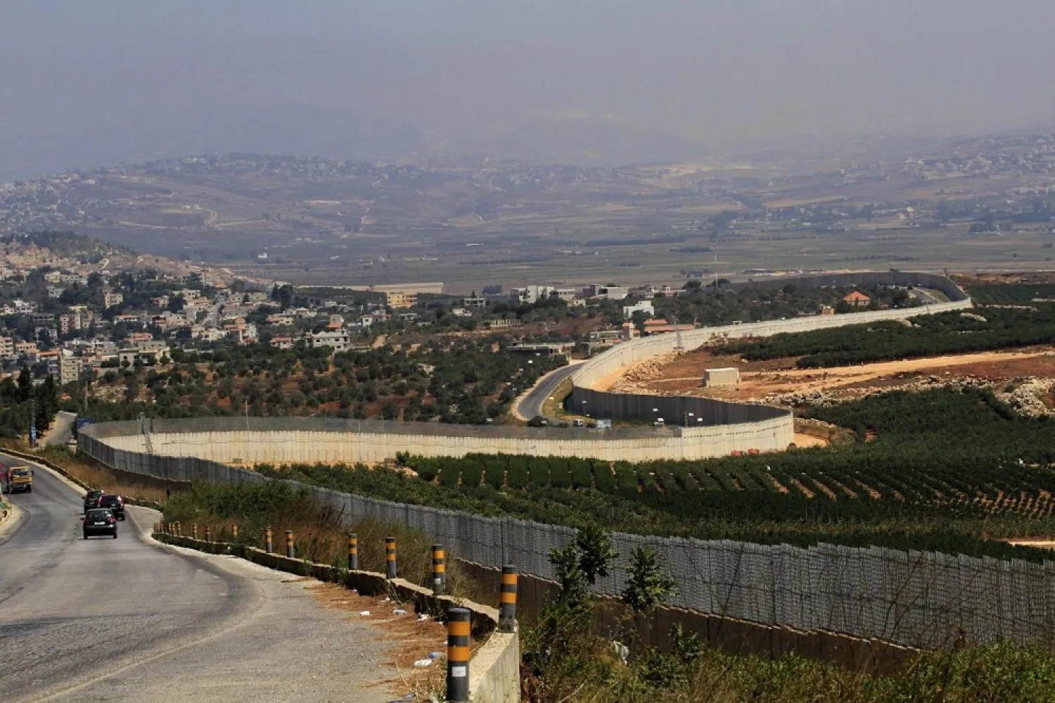 Vehicles drive along a border wall with Israel near the southern Lebanese village of Adaisseh on August 26. (AFP)