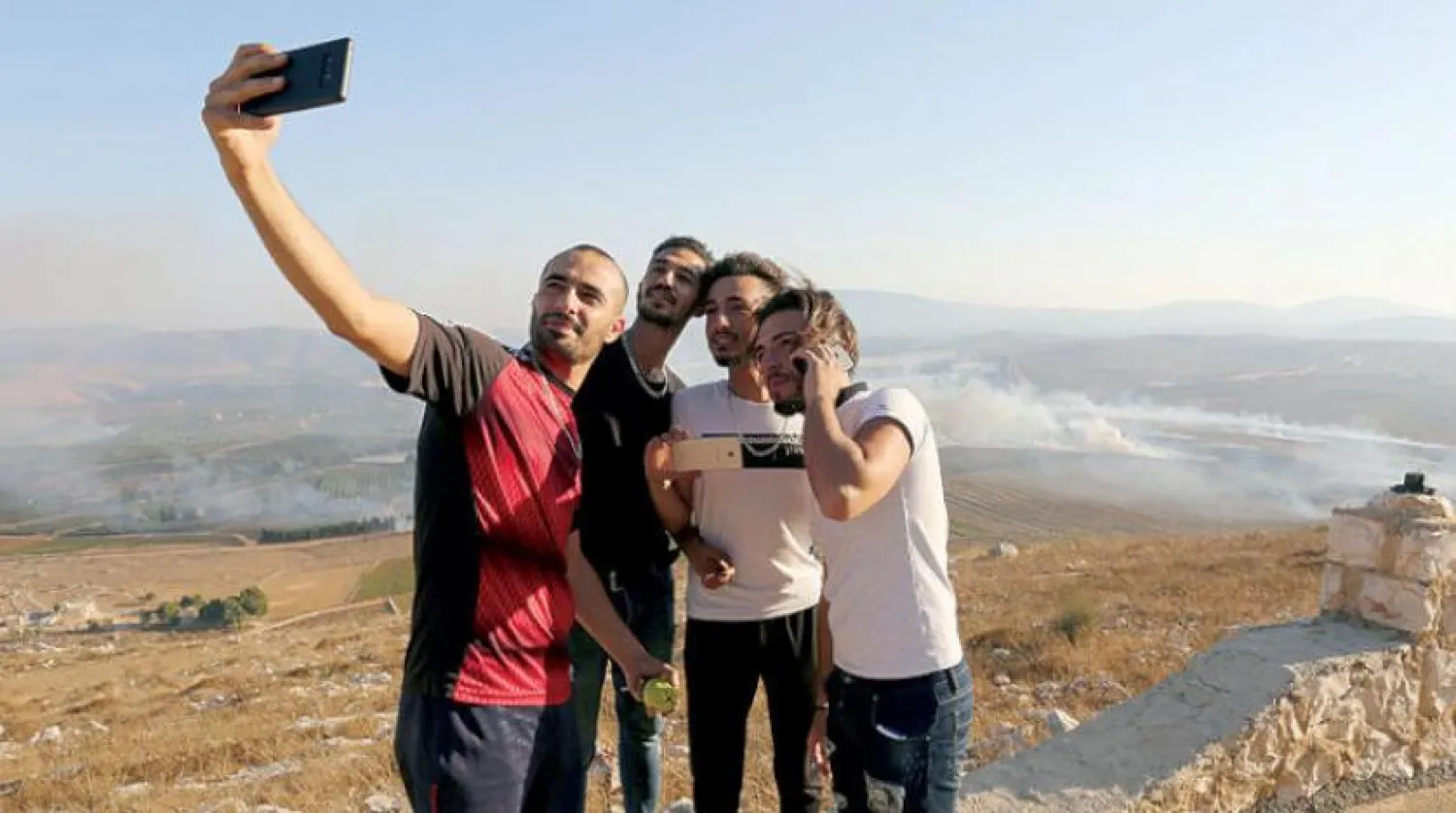 People take selfies as smoke rises from shells fired from Israel in Maroun al-Ras village, near the border with Israel, in southern Lebanon, September 1, 2019. REUTERS/Aziz Taher