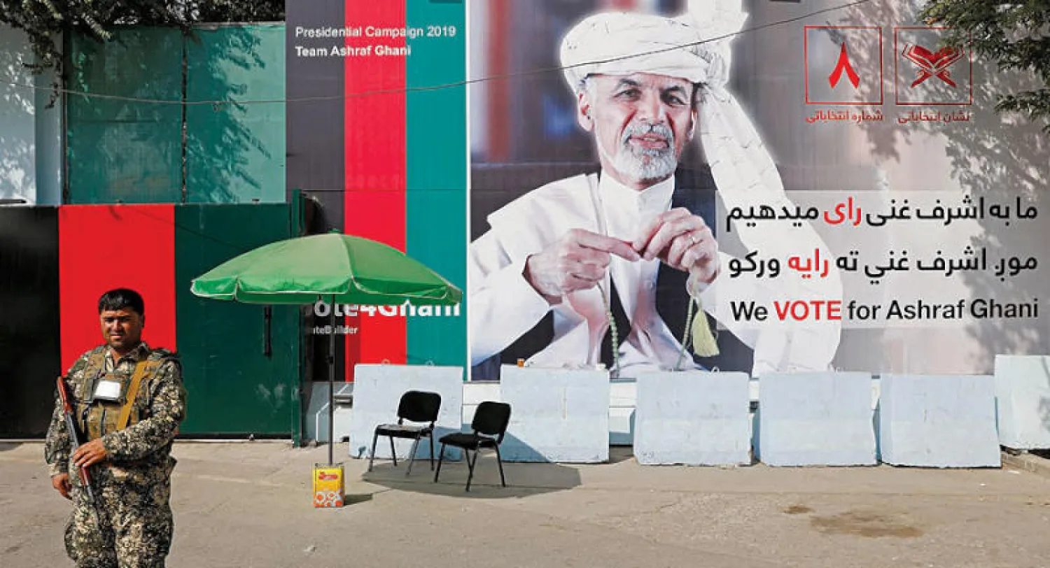 أحد أفراد قوات الأمن أثناء دورية حراسة أمام مؤسسة حكومية عليها ملصق دعائي للمرشح الرئاسي أشرف غني في كابل أمس (رويترز)