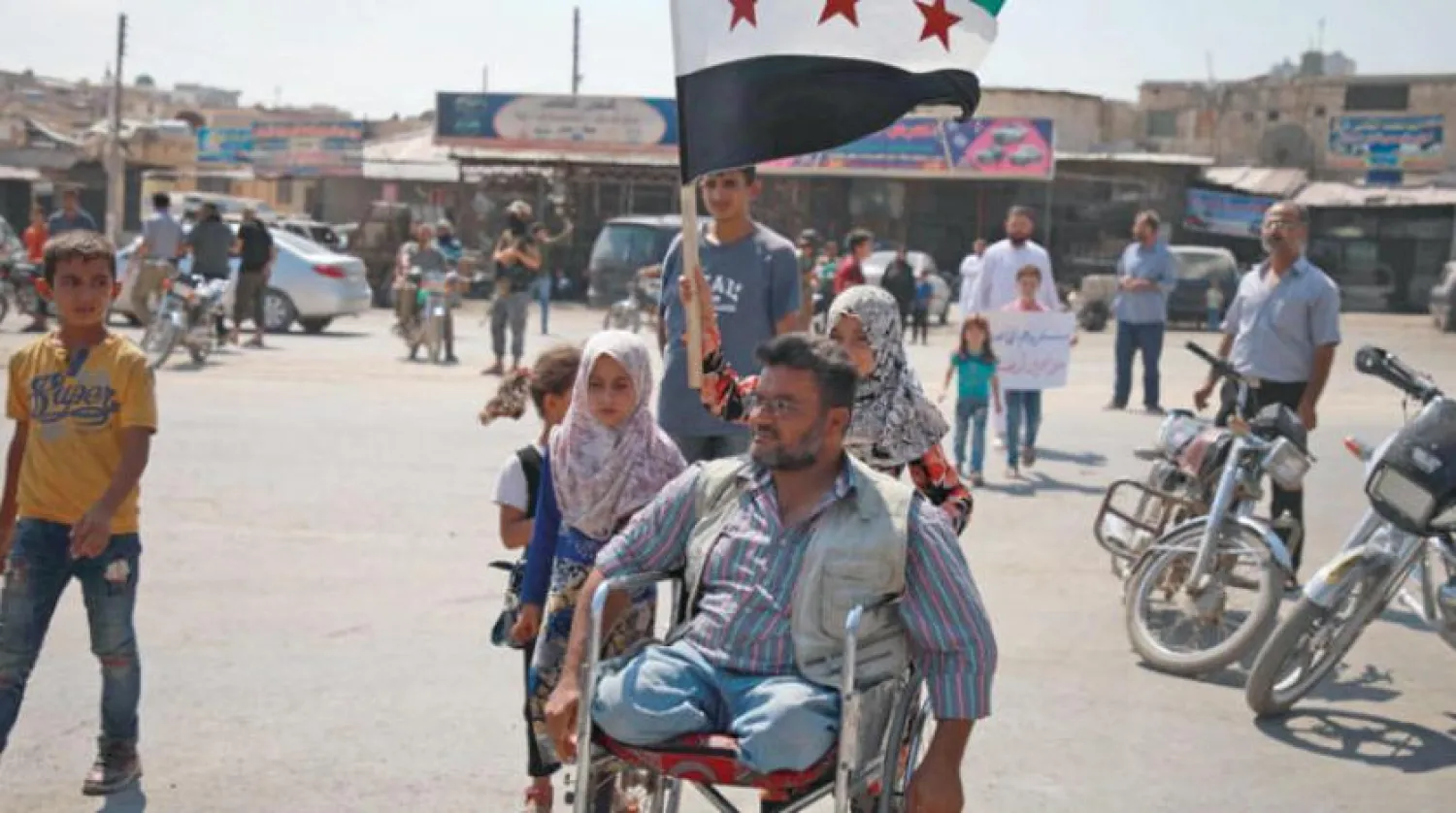 An amputee propels his wheelchair as a girl behind him raises the flag of the Syrian opposition during a demonstration against the Syrian regime and its ally Russia and calling for protection from the Turkish government, by the Bab al-Hawa crossing between Turkey and Syria's northwestern Idlib province on September 6, 2019. Aaref WATAD / AFP