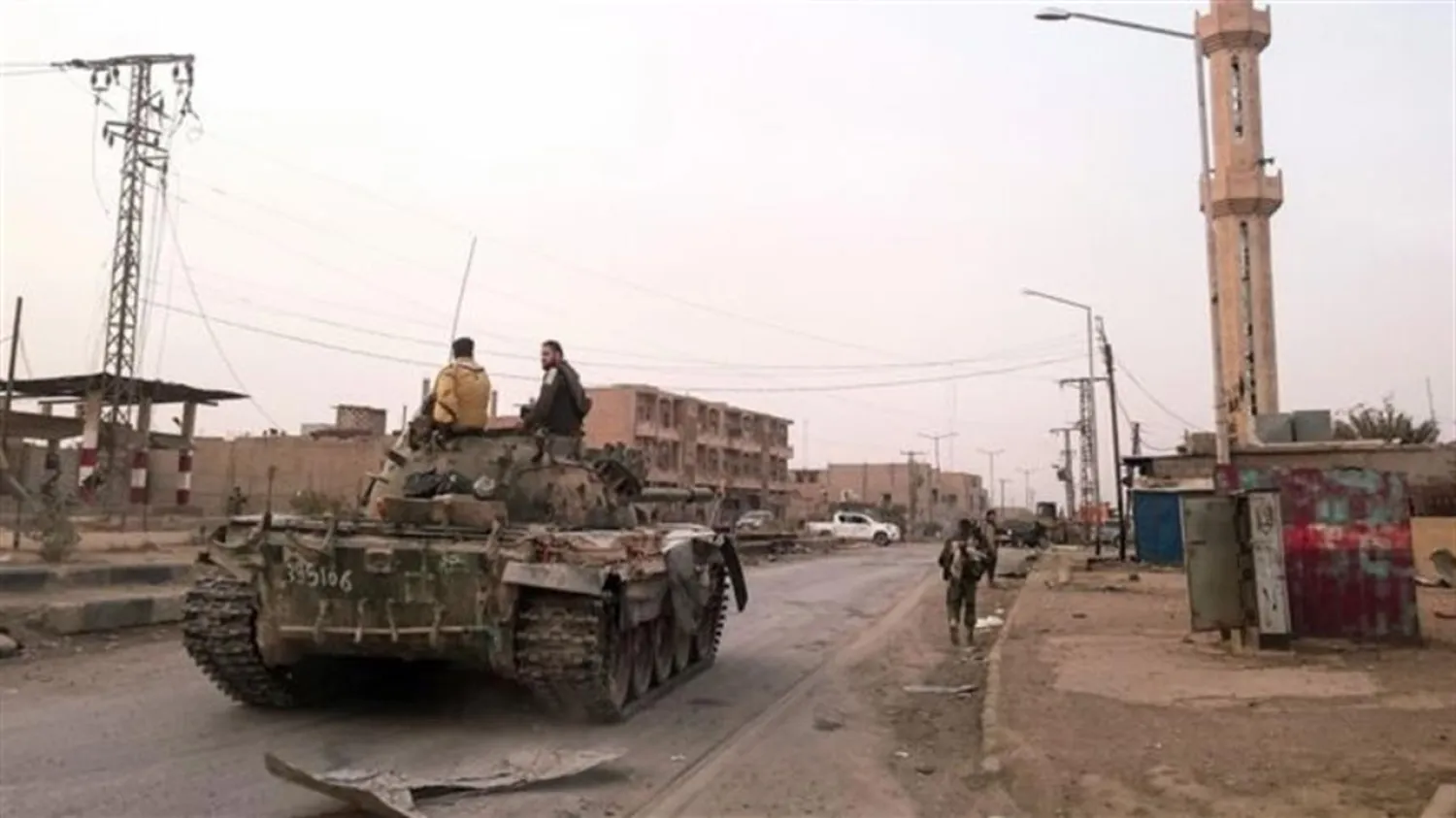 Members of the pro-Syrian government forces ride on a tank as it drives down a street in the Syrian border town of Albu Kamal | AFP