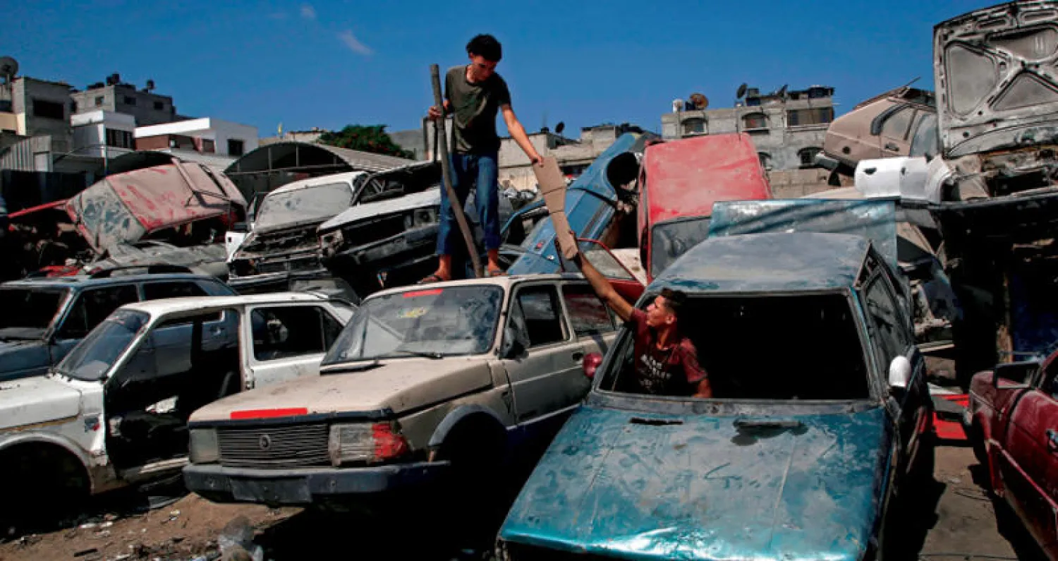 شابان فلسطينيان يجمعان قطعاً من سيارات خردة في ضاحية الشجاعية شرق مدينة غزة أمس (أ.ف.ب)