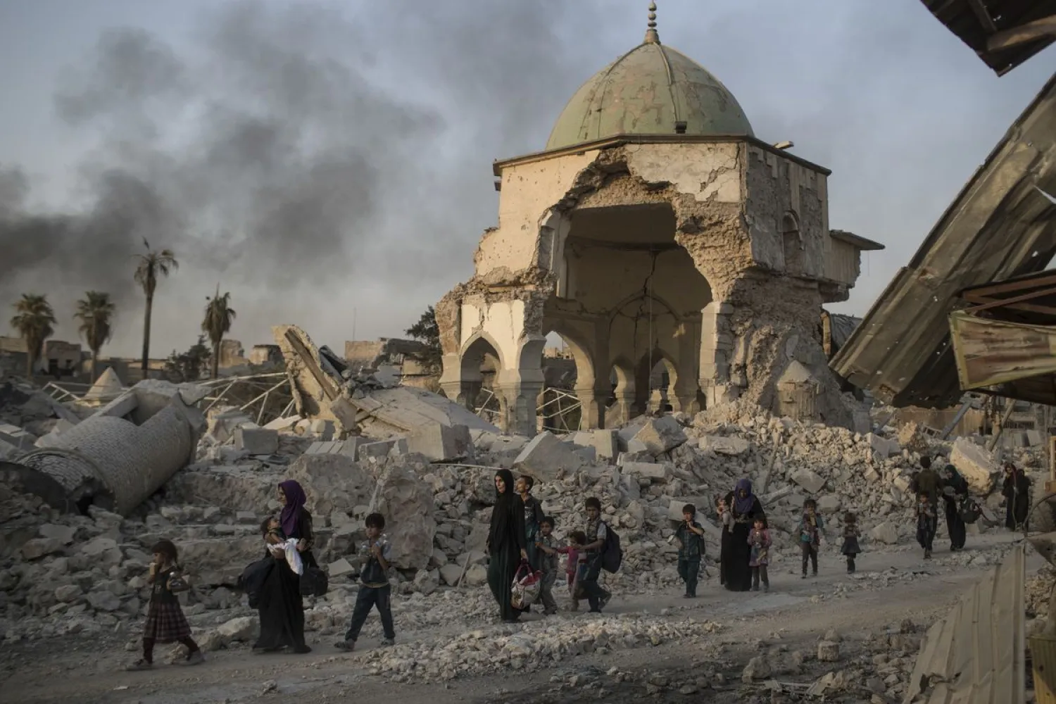 In this July 4, 2017, file photo, fleeing Iraqi civilians walk past the heavily damaged al-Nuri mosque as Iraqi forces continue their advance against ISIS militants in Iraq's Old City of Mosul. The United Nations' cultural agency says reconstruction of Al-Nouri Mosque in Iraq's city of Mosul is scheduled to start at the beginning of 2020. (AP Photo/Felipe Dana, File)
