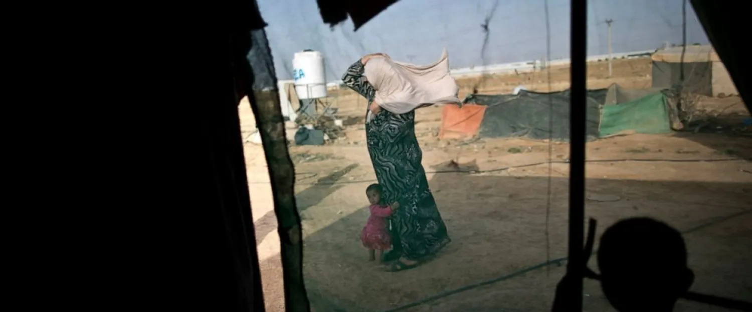 In this June 3, 2016 file photo, a Syrian refugee holds on to her headscarf against the wind while she and her daughter stand outside their tent at an informal tented settlement near the Syrian border, on the outskirts of Mafraq, Jordan. Nearly a year after Jordan opened its main border crossing for Syrian refugees to go home, few are taking up the offer. Afraid to return home, unable to earn a decent living in Jordan and unwanted by the West, refugees are trapped in a cycle of poverty and debt while straining the resources of a country that is already struggling to meet the needs of its own population. (AP Photo/Muhammed Muheisen, File)