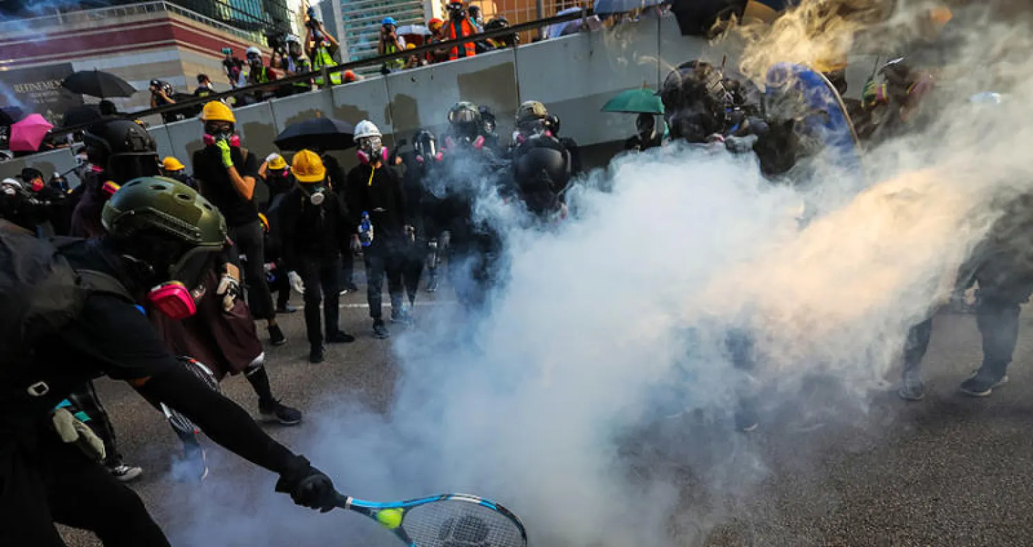 متظاهر يعيد قنبلة غاز مسيل للدموع للشرطة بمضرب تنس في هونغ كونغ أمس  (إ.ب.أ)