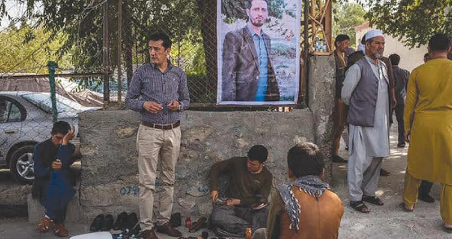 أفغان يتطلعون إلى صورة أكبر فاضليار الذي دفن في قريته بمقاطعة باروان شمال كابل (نيويورك تايمز)