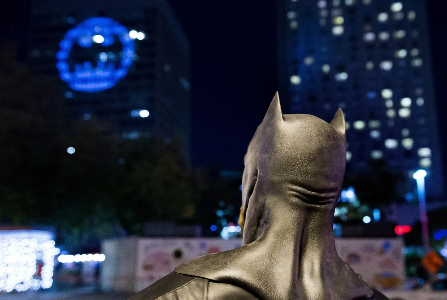 A man dressed as Batman looks up towards the Batman signal projected onto a building to celebrate Batman Day in Montreal, Saturday, September 21, 2019. (AP)