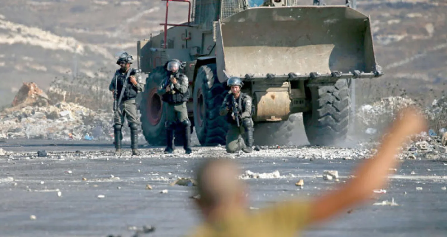 جنود إسرائيليون يوجهون أسلحتهم نحو شاب فلسطيني يشارك في احتجاجات قرب رام الله بالضفة الغربية أمس تضامناً مع الأسرى في سجون الاحتلال (أ.ف.ب)