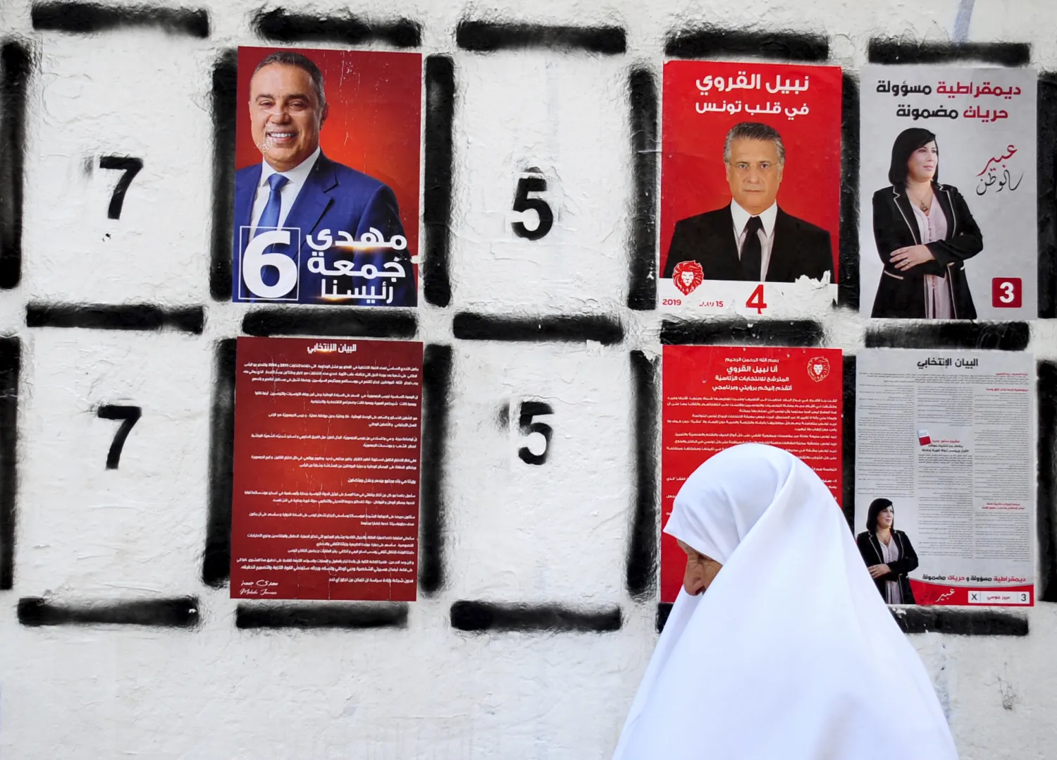 In this September 4, 2019 file photo, a woman walks past a wall of campaign posters in Tunis, Tunisia. (AP Photo/Hassene Dridi, File)