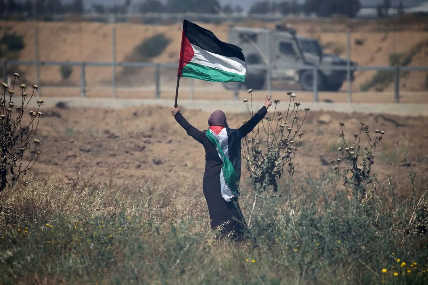 FILE PHOTO: A woman holding a Palestinian flag gestures in front of Israeli forces during a protest marking the 71st anniversary of the 'Nakba', at the Israel-Gaza border fence, in the southern Gaza Strip May 15, 2019. REUTERS/Ibraheem Abu Mustafa/File Photo