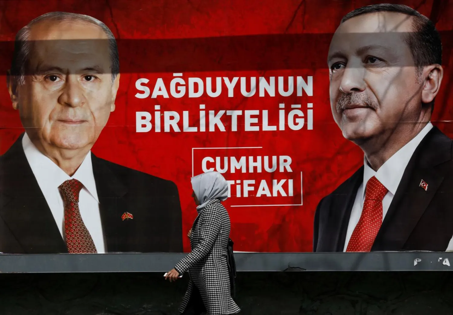 FILE PHOTO: A woman walks past a banner for the upcoming local elections in Ankara, Turkey, March 27, 2019. Banner with pictures of Turkish President Tayyip Erdogan and Devlet Bahceli, leader of Nationalist Movement Party (MHP), reads: "People's Alliance: The unity of common sense." REUTERS/Umit Bektas