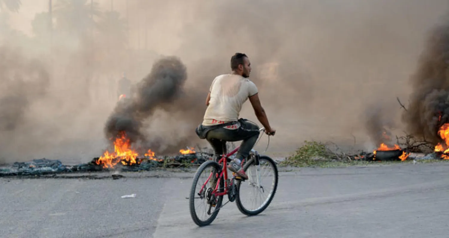 صورة وزعت أمس لعراقي يستقل دراجته الهوائية في شارع مسدود بإطارات مشتعلة ببغداد (إ.ب.أ)