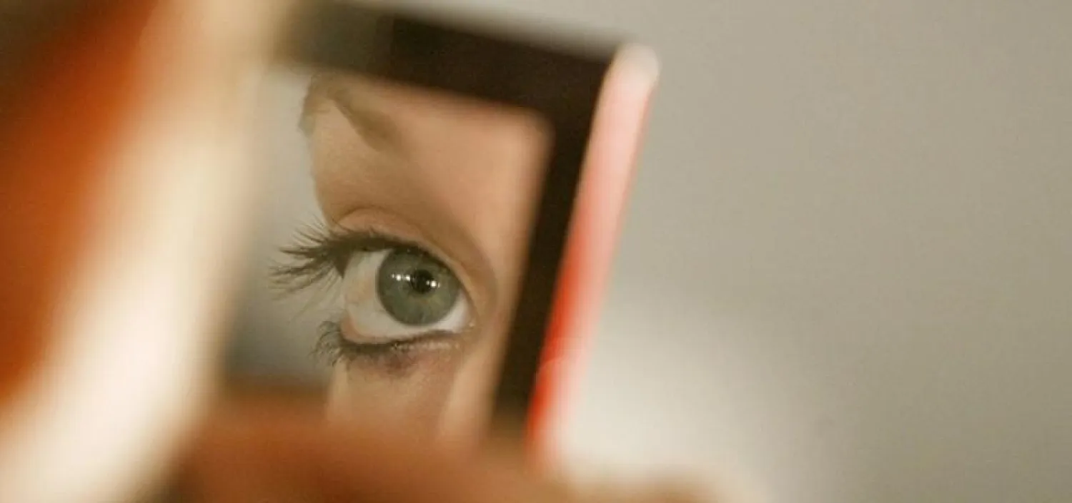 امرأة تنظر إلى عينها بالمرآة (رويترز)