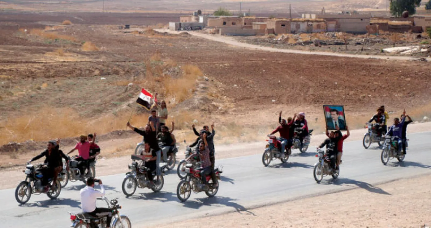 عناصر من قوات النظام السوري ومواطنون يرفعون العلم الرسمي في تل تمر شرق الفرات أمس (أ.ب)