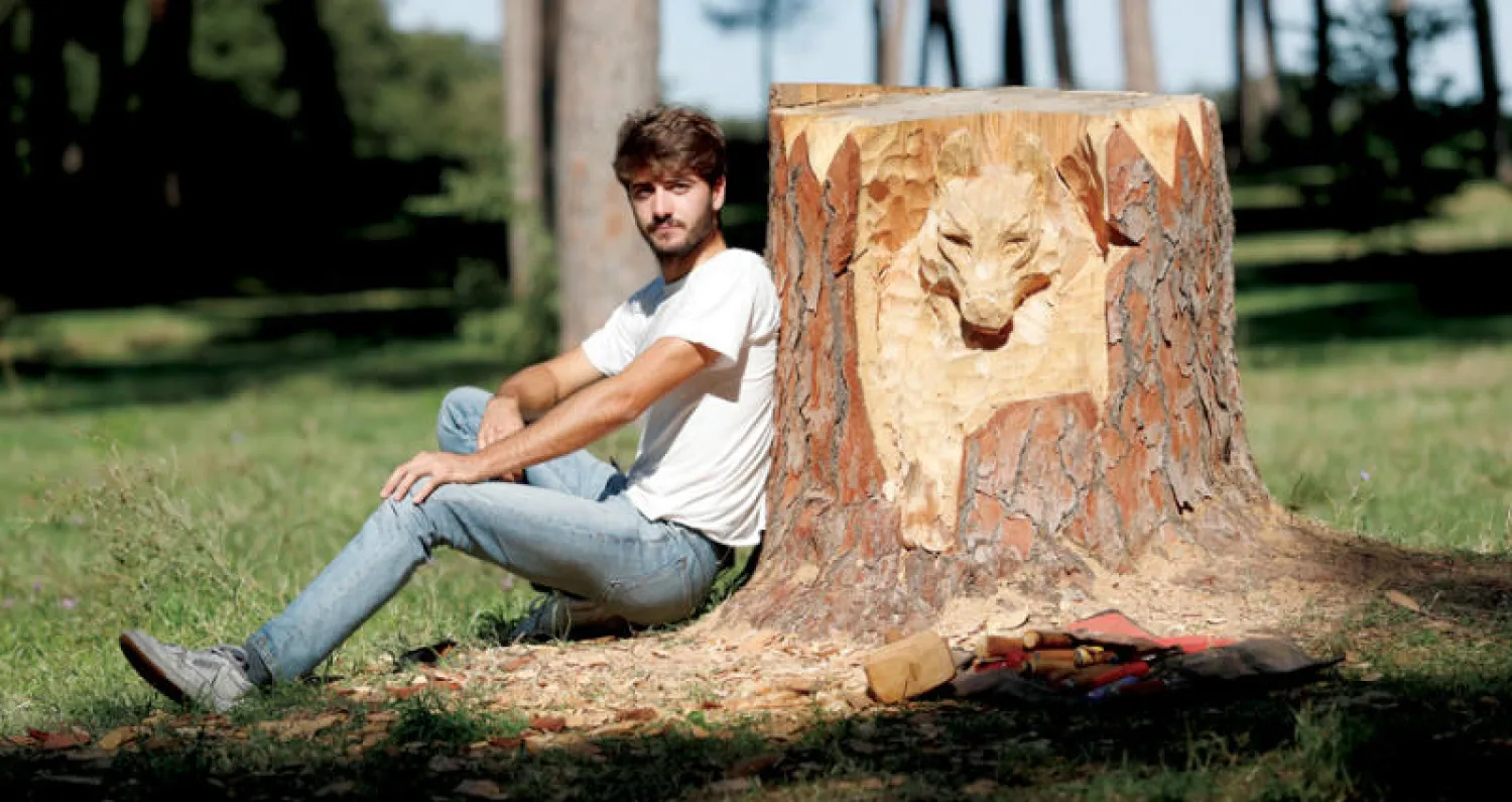 النحات الإيطالي أندريا جانديني يجلس إلى جوار نحت لوجه ذئب على جذع شجرة ميتة في روما (رويترز)