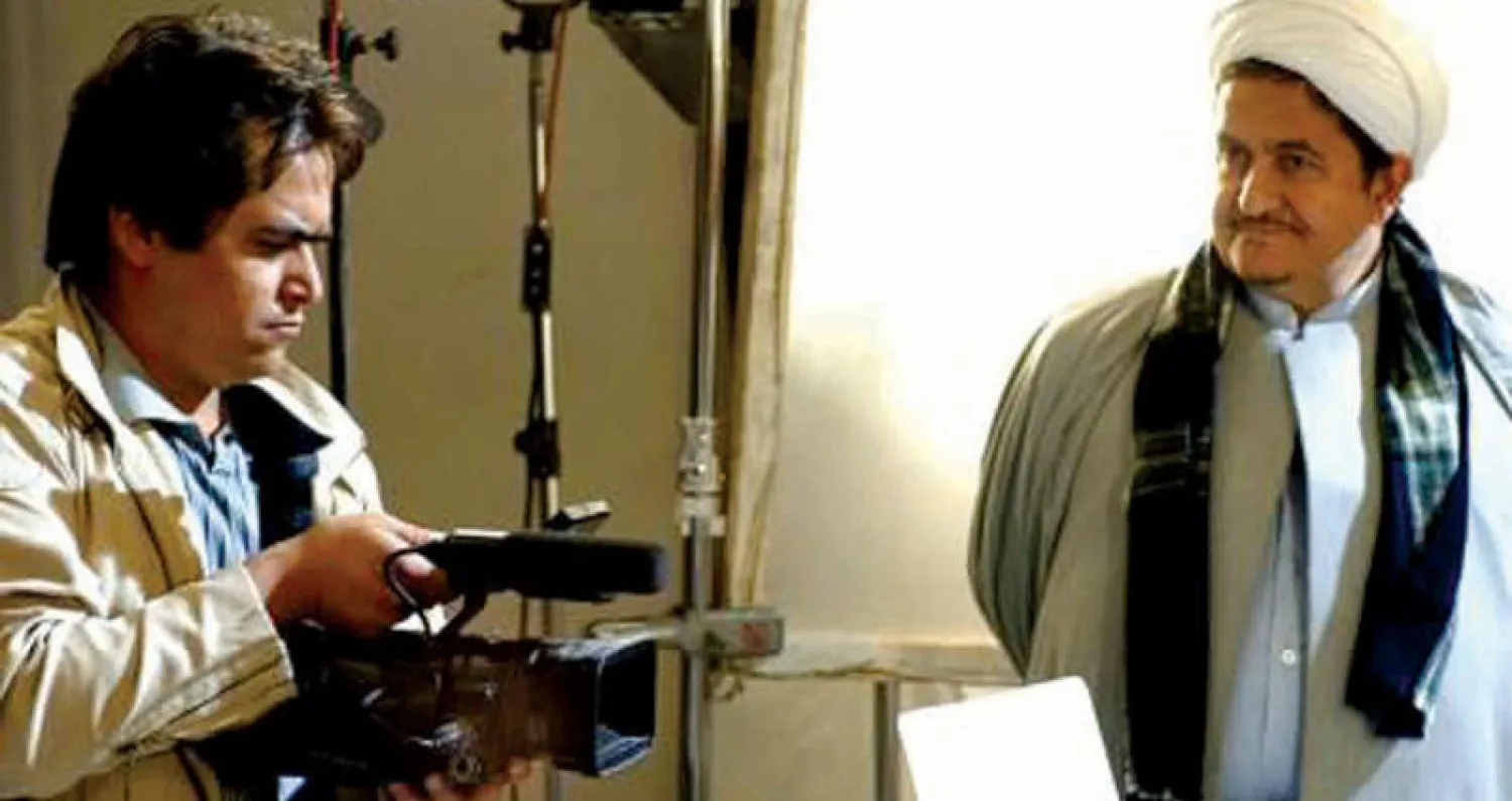 روح الله زم یمسك بكاميرا تصوير إلى جانب والده محمد علي زم الذي شغل منصب رئيس القسم الفني  في «منظمة الدعاية الإسلامية» التابعة لمكتب المرشد الإيراني (يوتيوب)