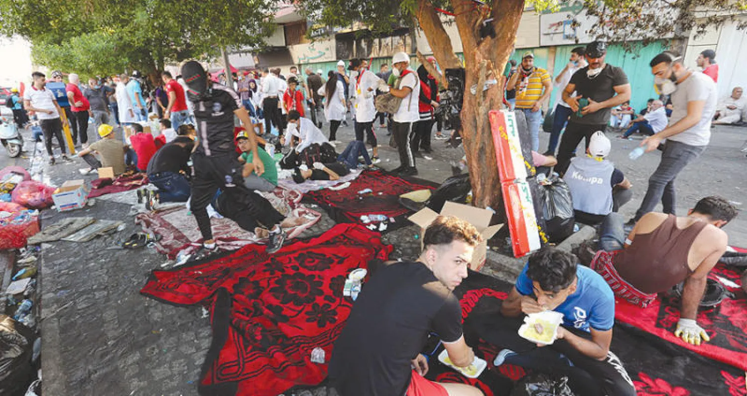 محتجون عراقيون يفترشون الأرض أمس خلال الاحتجاجات المستمرة في ساحة التحرير (إ.ب.أ)