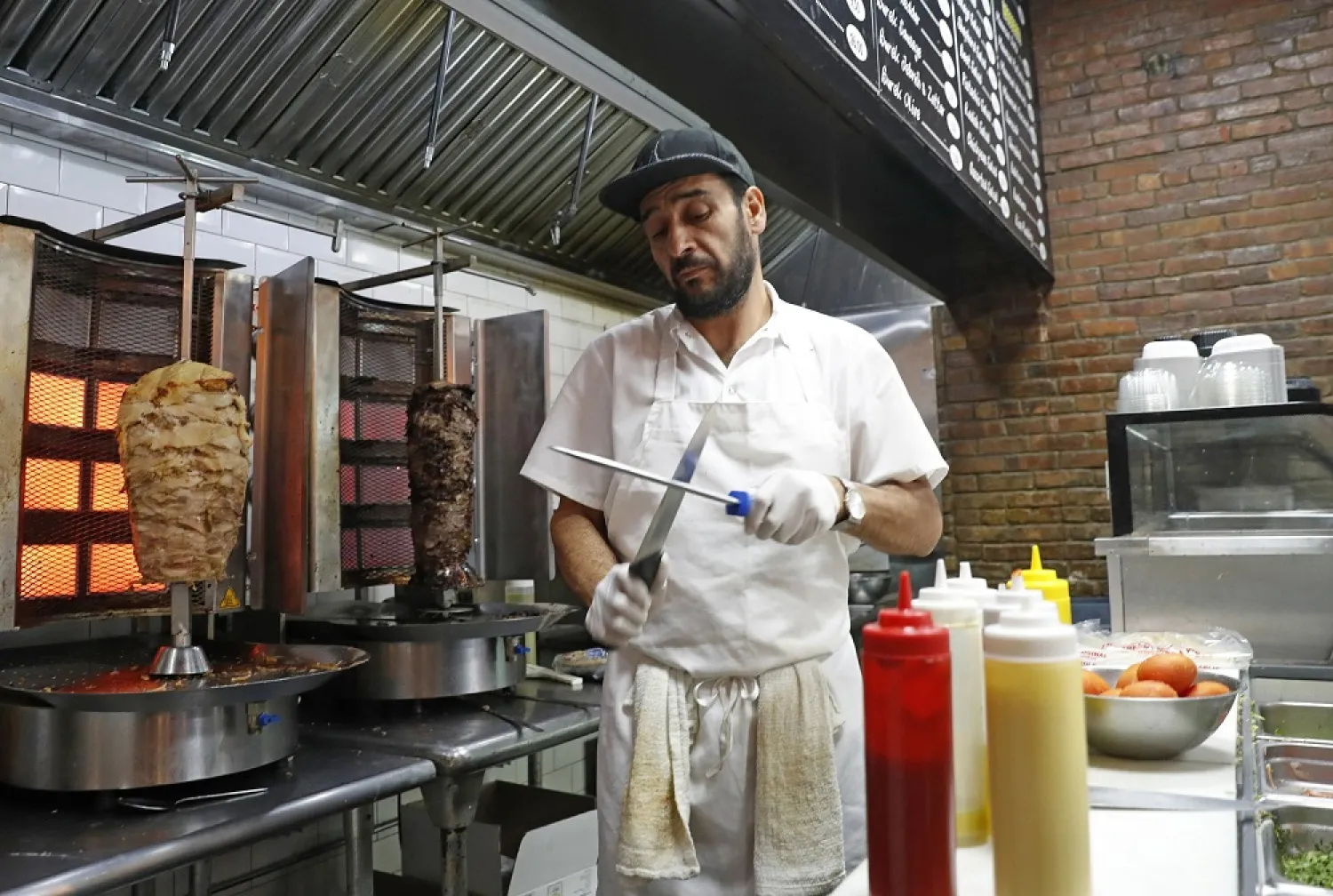 Chef Diaa Alhanoun sharpens his knives between serving customers, while skewered pieces of cooked chicken and beef known as ‘shawarma’ are kept warm at his restaurant in New York. (AP)