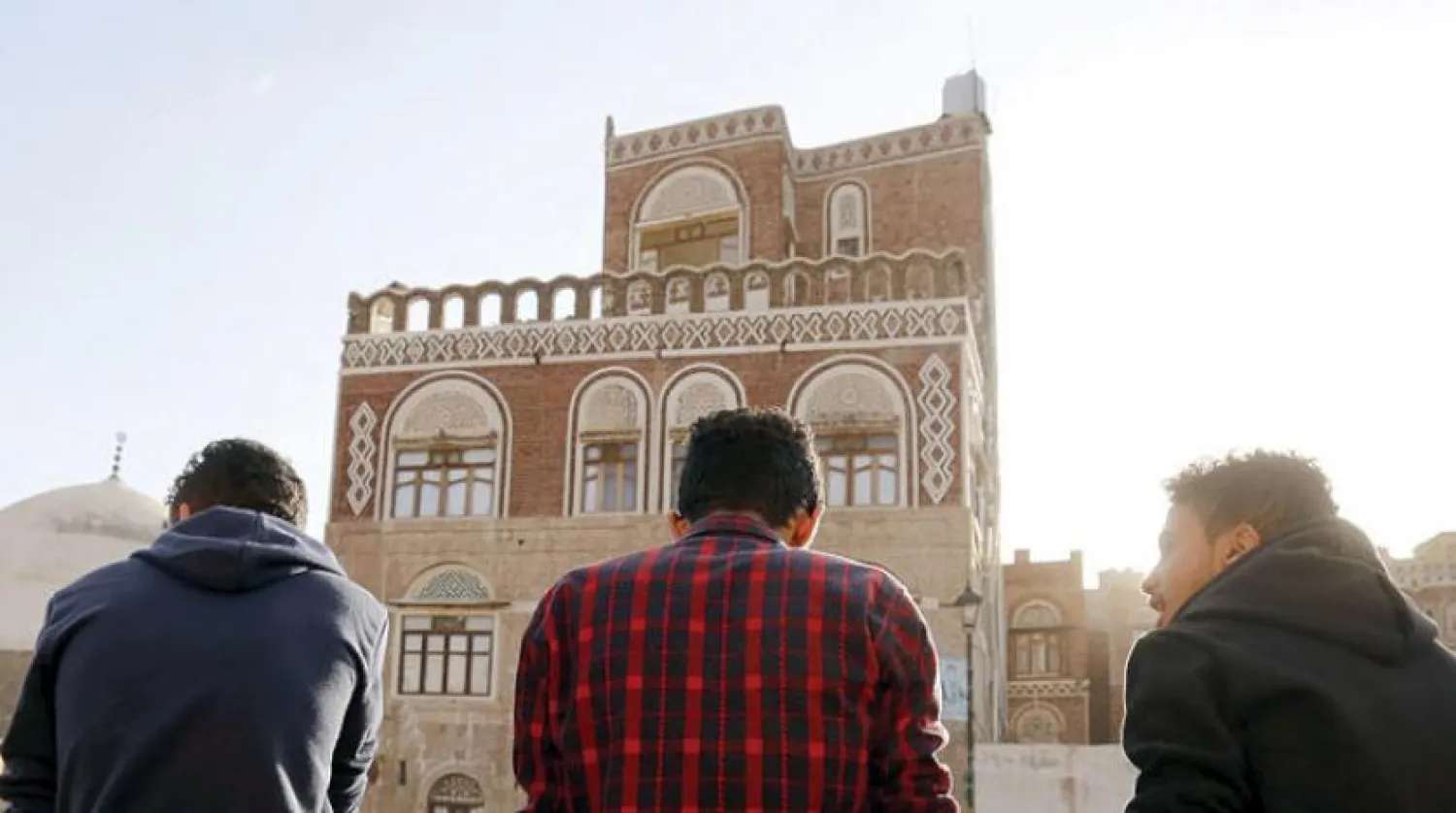 Yemenis speak as they sit facing one of Sanaa's old city buildings (EPA)

