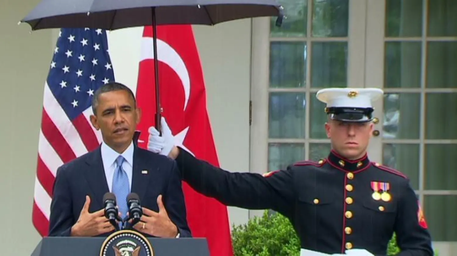 عنصر من المارينز يحمل المظلة فوق رأس الرئيس الأميركي السابق باراك أوباما (سي إن إن)