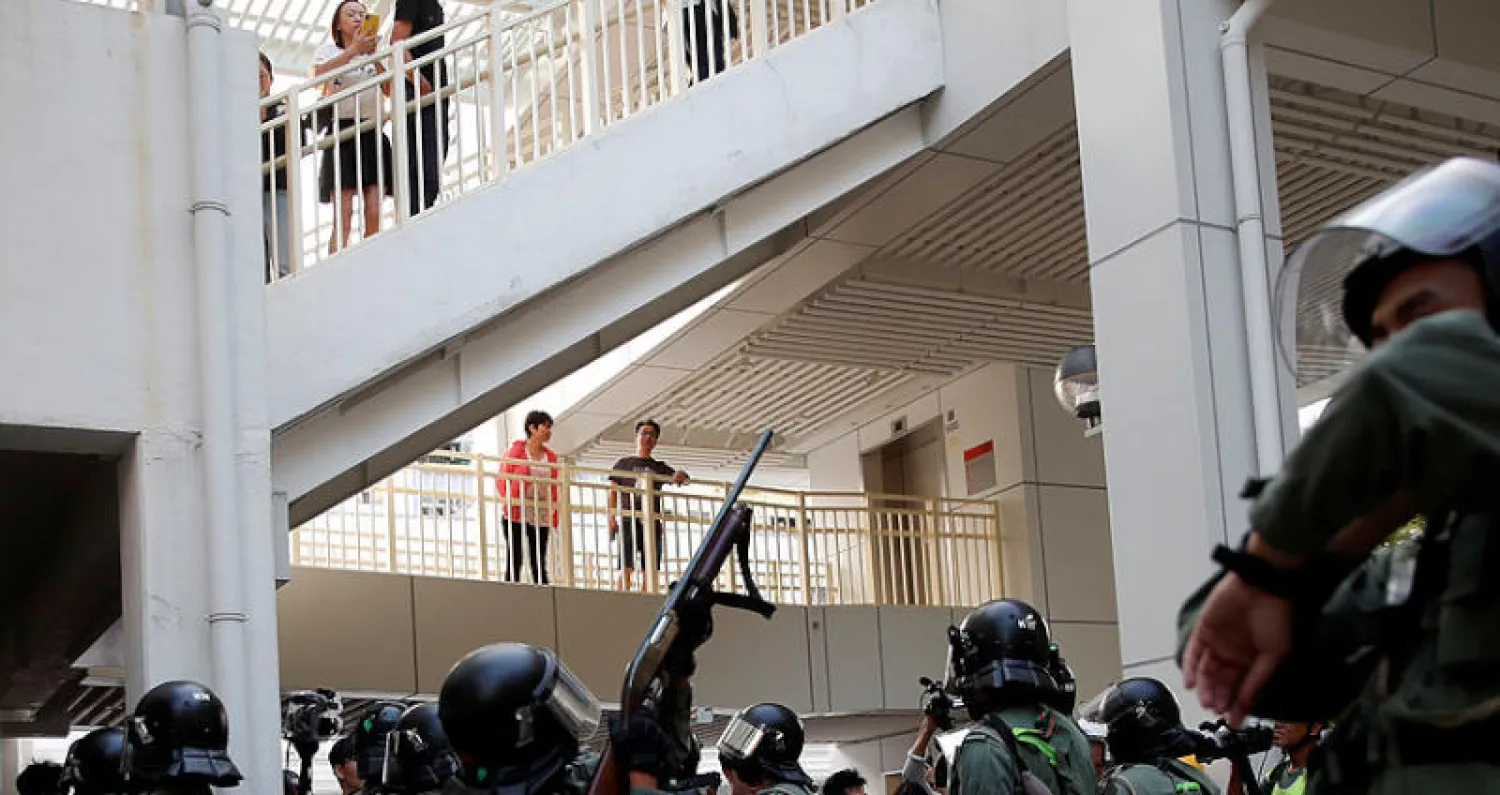 شرطي يوجه سلاحه نحو المتظاهرين في هونغ كونغ أمس (رويترز)