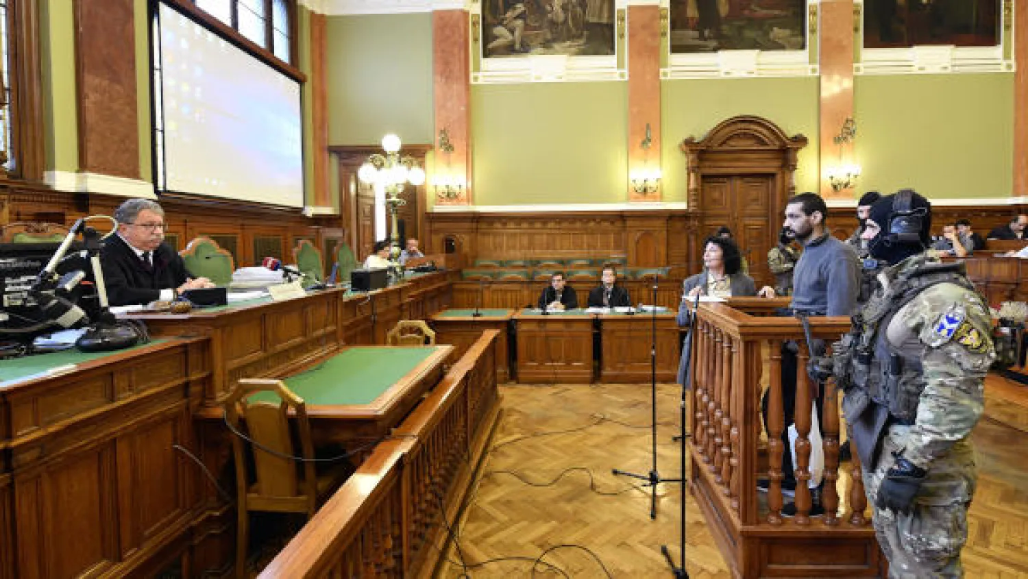A Syrian man identified as Hassan F. stands on a podium as he arrives at the Metropolitan Court in Budapest, Hungary, Wednesday, Nov. 13, 2019. Prosecutors said the 27-year-old man identified only as Hassan F. participated in the beheading of a religious leader in the city of al-Sukhnah in Homs province and was also involved in the killings of at least 25 people. (Zsolt Szigetvary/MTI via AP)

