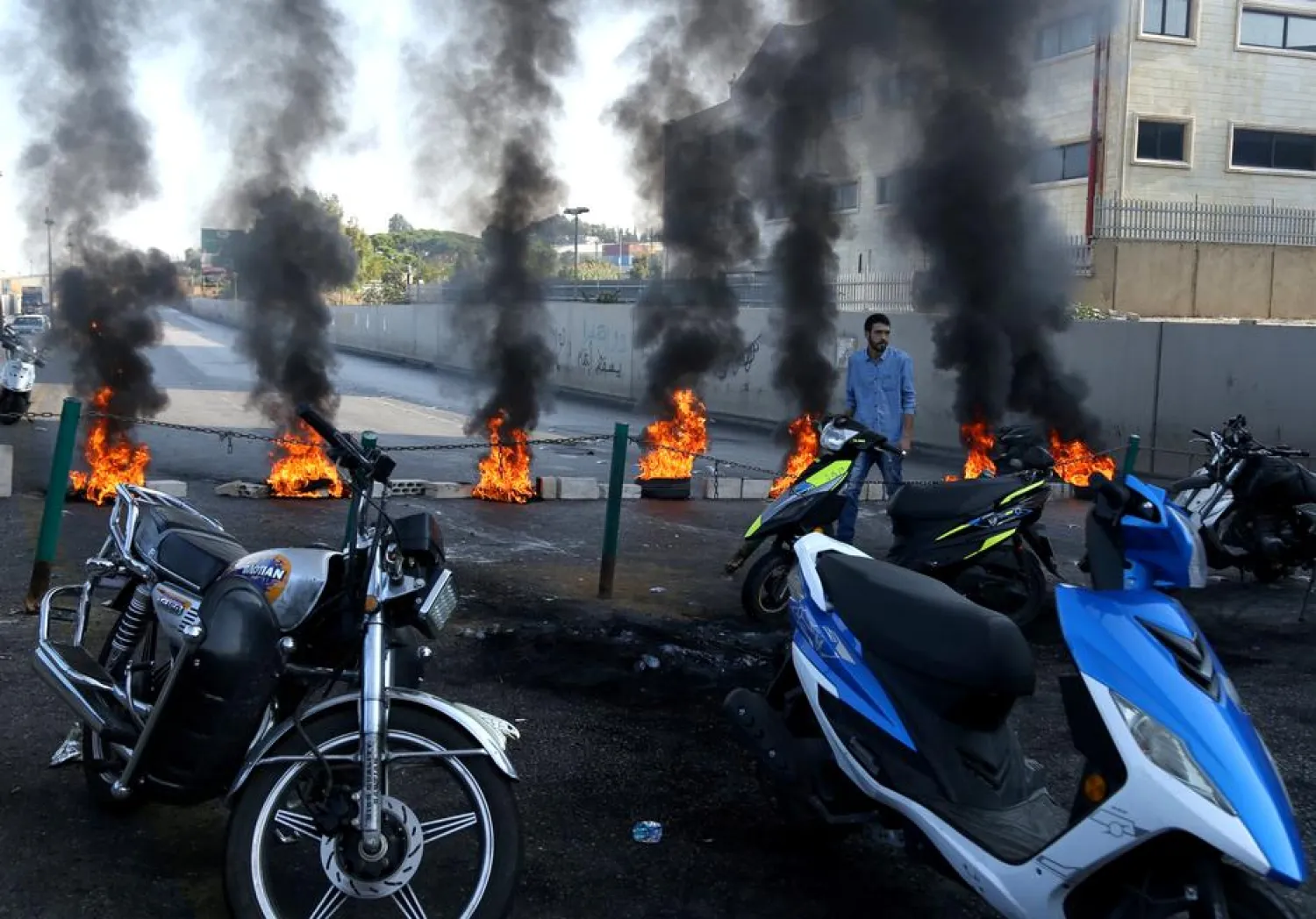 A demonstrator walks past a closed road by burning tires during ongoing anti-government protests, in Khaldeh, Lebanon November 13, 2019. REUTERS/Alaa Kanaan
