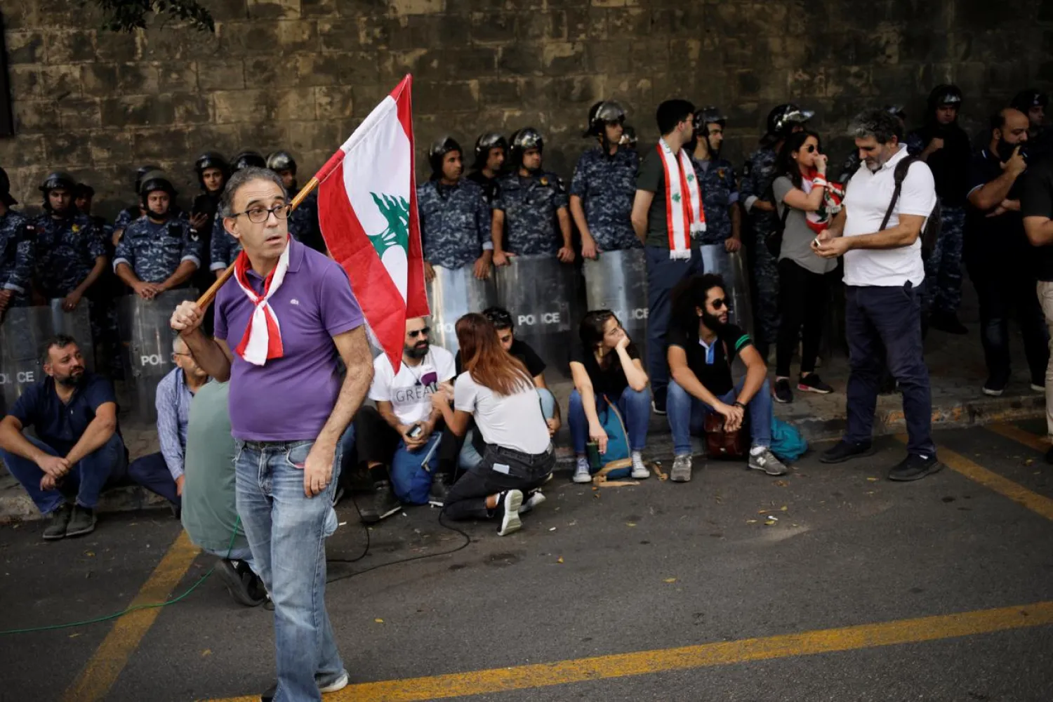 A protester carries a flag as he stands in front of police officers outside of the Ministry of Foreign Affairs and Emigrants during a protest in Beirut, Lebanon November 9, 2019. REUTERS/Andres Martinez Casares