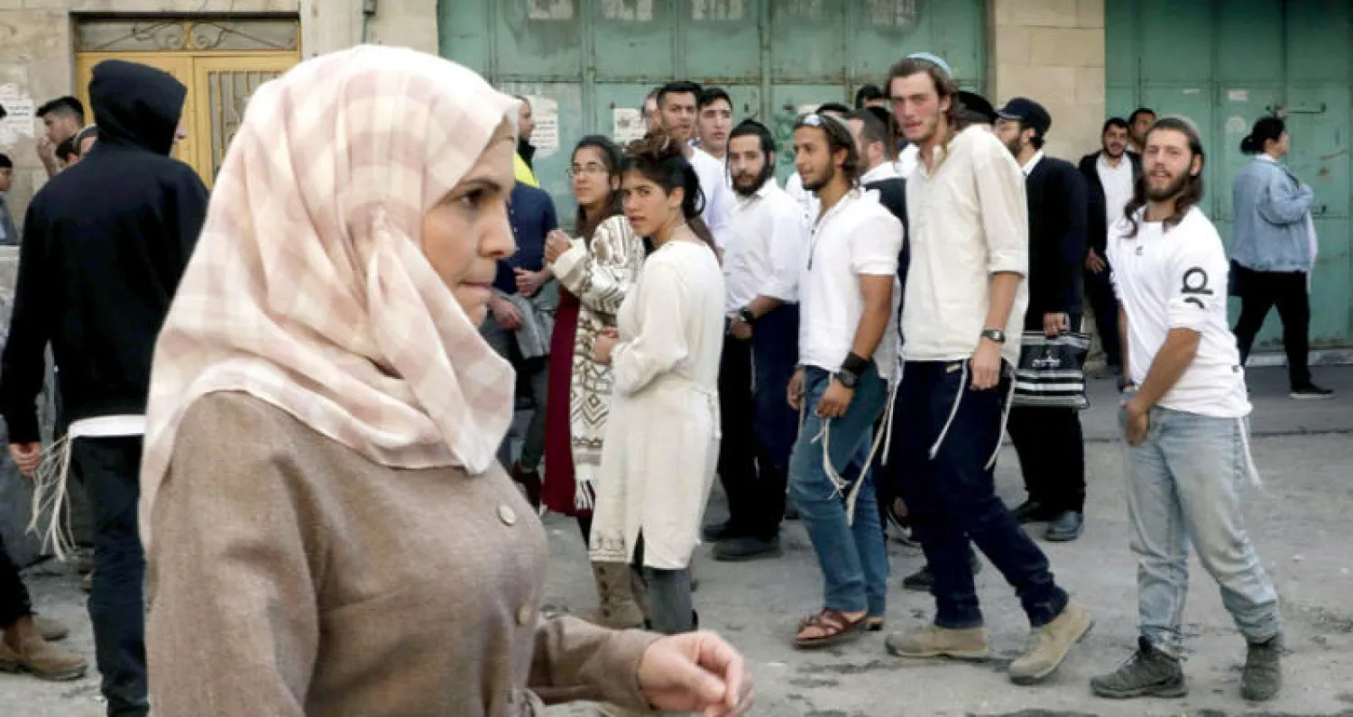 فلسطينية تمر قرب مجموعة من المستوطنين المتطرفين في طريقهم لاقتحام الحرم الإبراهيمي أمس (أ.ف.ب)