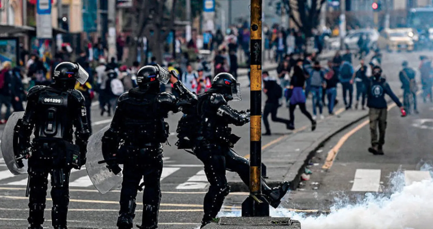أحد أفراد مكافحة الشغب يُبعد قنبلة غاز مسيل للدموع في بوغوتا أول من أمس (أ.ف.ب)