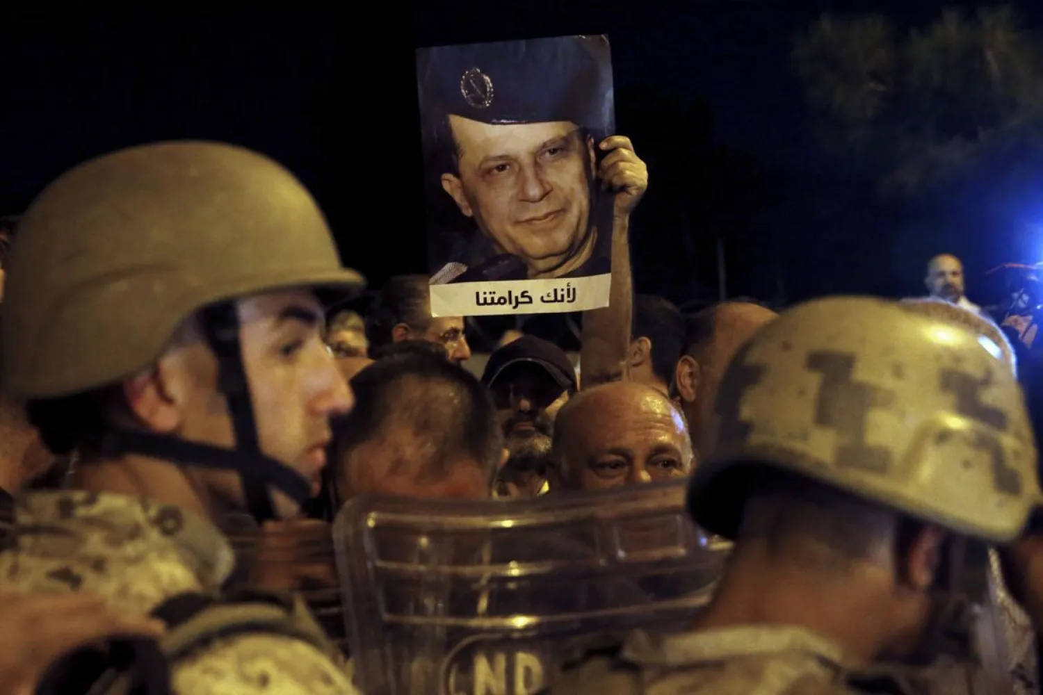 A supporter of Lebanese President Michel Aoun holds up his picture with Arabic that read "Because you are our dignity," as Lebanese republican guards stand guard during a protest near the presidential palace in the Beirut suburb of Baabda, Lebanon, Tuesday, Nov. 26, 2019. Dozens of people are marching to show their support for Aoun and his proposed political reforms that come after more than five weeks of widespread anti-government demonstrations. (AP Photo/Bilal Hussein)