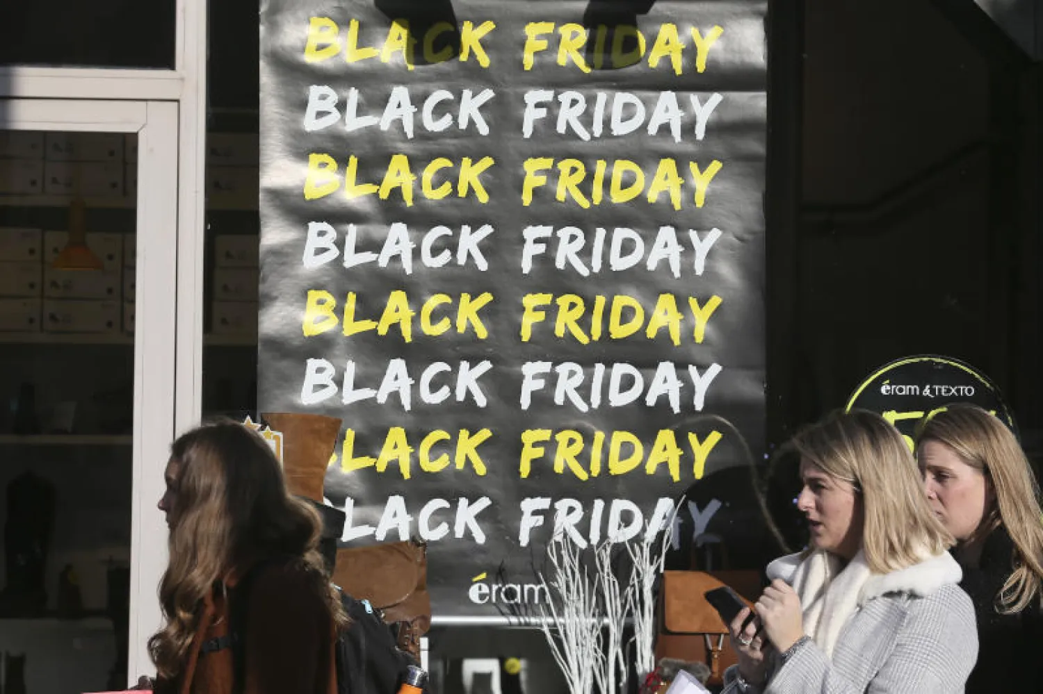 نساء يسرن إلى جانب ملصق يروّج ليوم «الجمعة السوداء» في رين بغرب فرنسا (أ.ب)