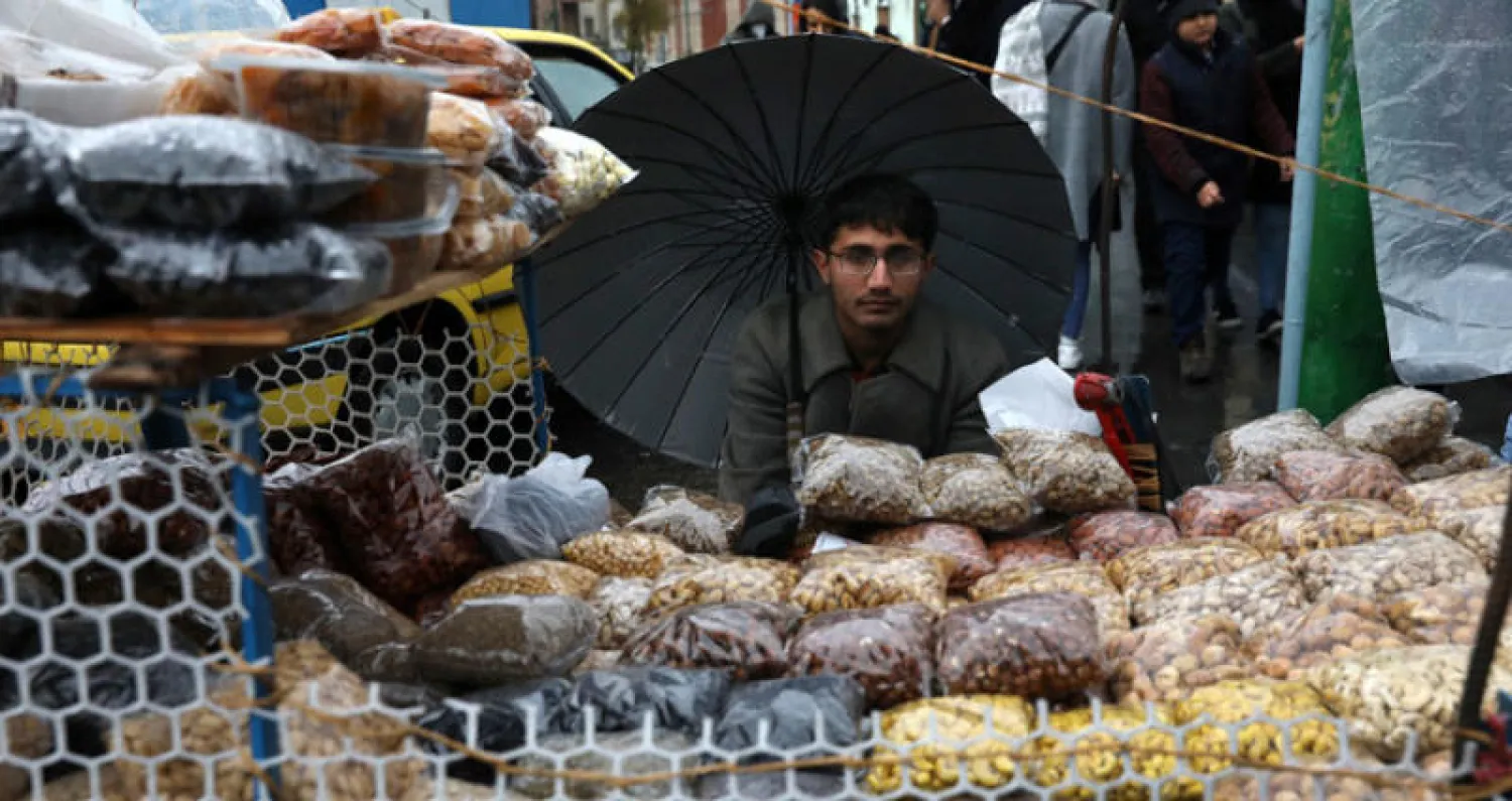 بائع يحتمي من الأمطار في العاصمة الإيرانية أمس (أ.ب)