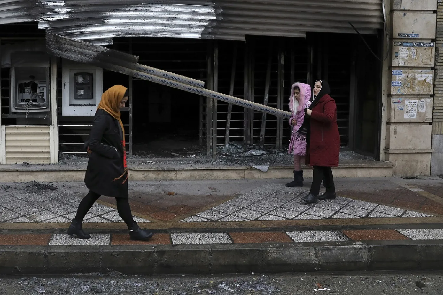 People walk past a bank that was burned in recent protests in Shahriar, Iran. (AP)