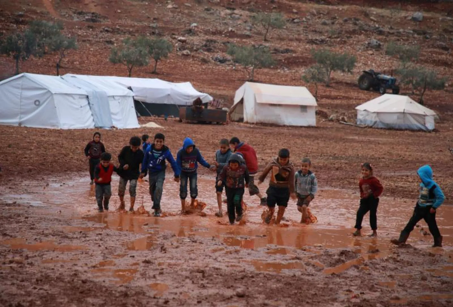 أولاد يلعبون في بركة ماء نتجت عن أمطار غزيرة، في مخيم للنازحين قرب بلدة كللي في محافظة إدلب (أ.ف.ب)