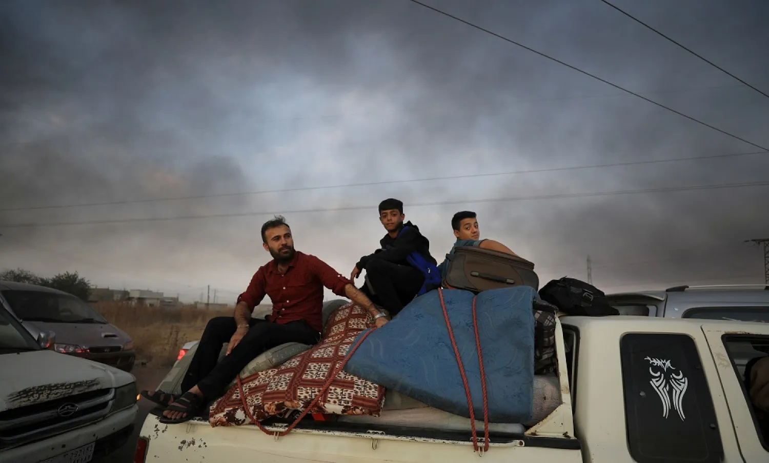 A man and two boys sit on belongings at the back of a truck as they flee Ras al-Ain, Syria, Oct. 9, 2019, with smoke billowing in the background during a Turkish offensive. (Reuters)