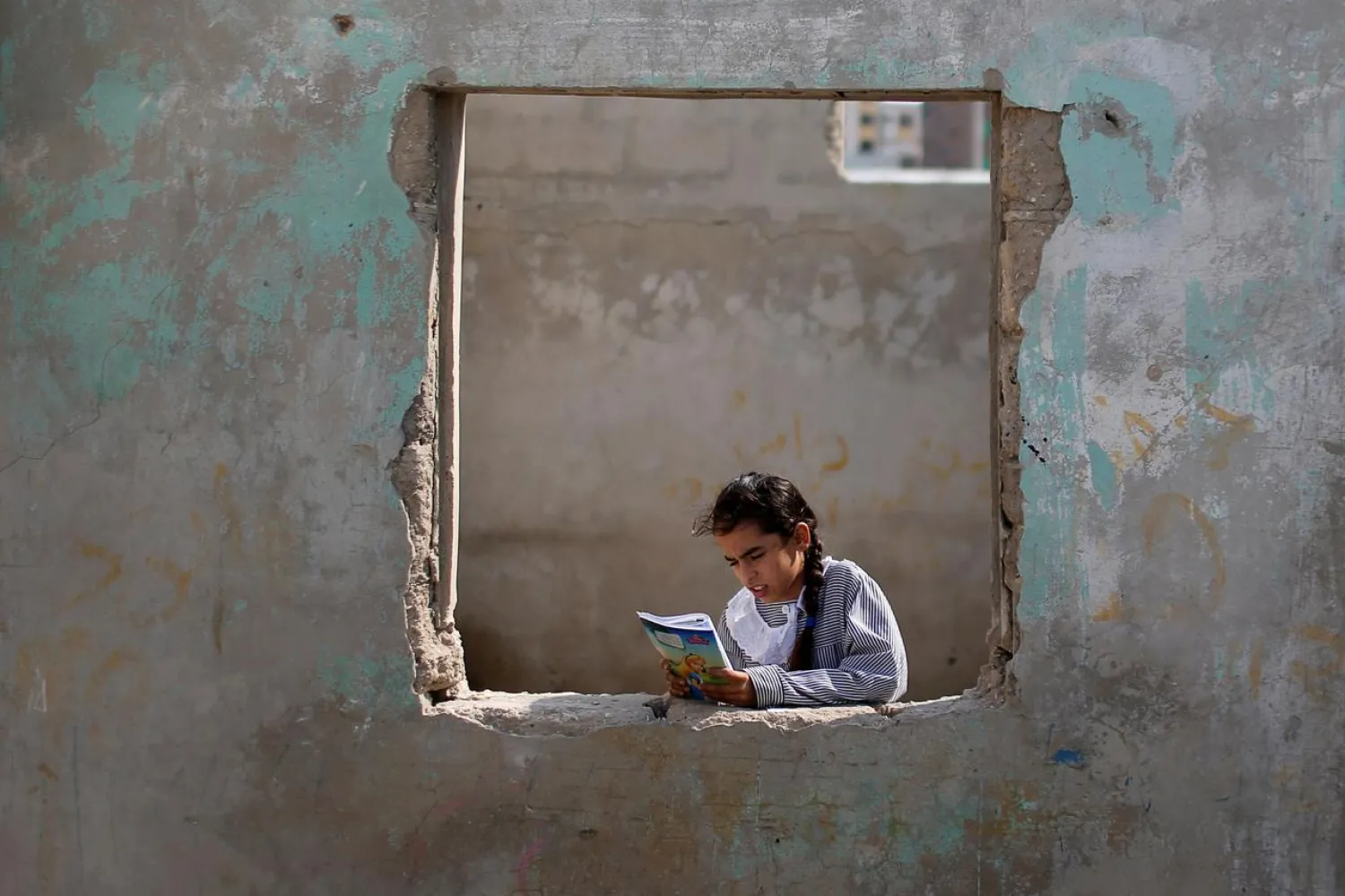 A Palestinian UNRWA schoolgirl holds her book as she stands by a window outside her family home in Al-Shati refugee camp in Gaza City October 23, 2019. (Reuters)