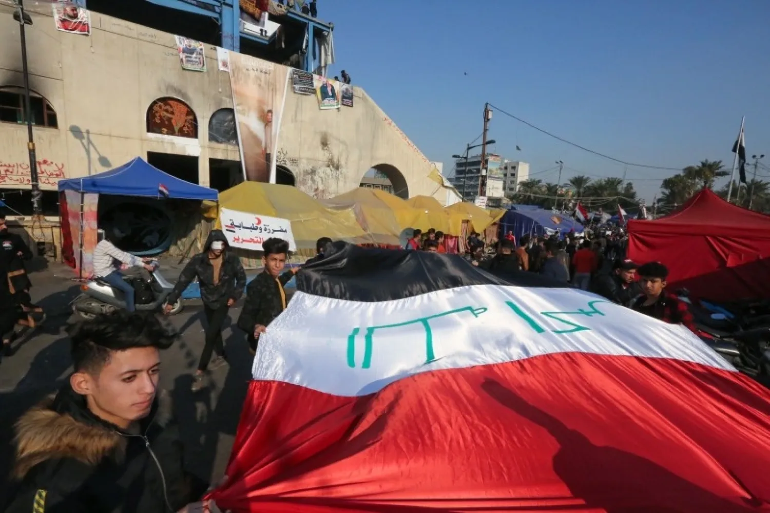 Iraqi anti-government protesters carry a large national flag during ongoing demonstrations in the capital Baghdad's Tahrir square | AFP