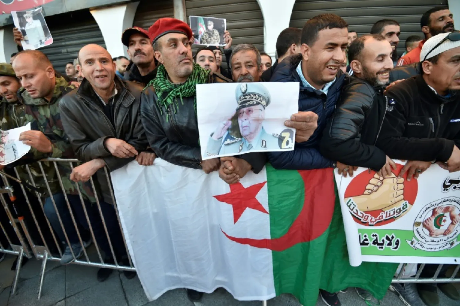 People stand with national flags and portraits of Algeria's late military chief Lieutenant general Ahmed Gaid Salah as they gather outside the People's Palace during his funeral in Algiers on Wednesday | AFP