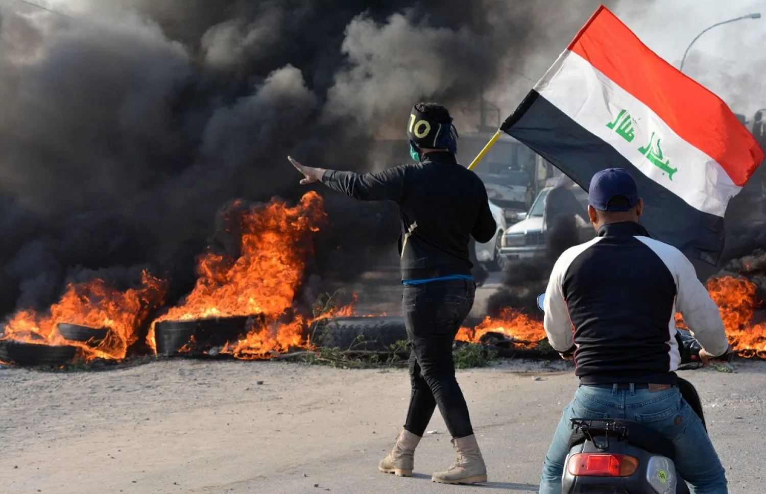 A demonstrator holds an Iraqi flag near burning tires during ongoing anti-government protests in Nassiriya, Iraq, Nov. 24, 2019. (Reuters)